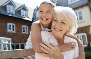 Granddaughter Hugging Grandmother On Bench During Visit To Retirement Home