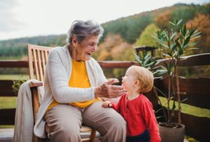 Elderly woman sitting with a toddler great-grandchild on a terrace in autumn.